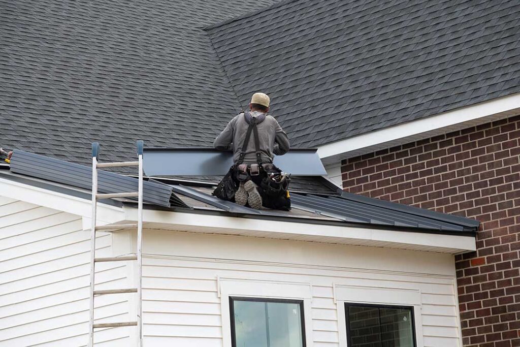 A pair of hands holding up two asphalt shingles side by side on a residential roof for comparison.