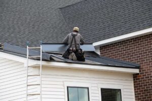 A pair of hands holding up two asphalt shingles side by side on a residential roof for comparison.