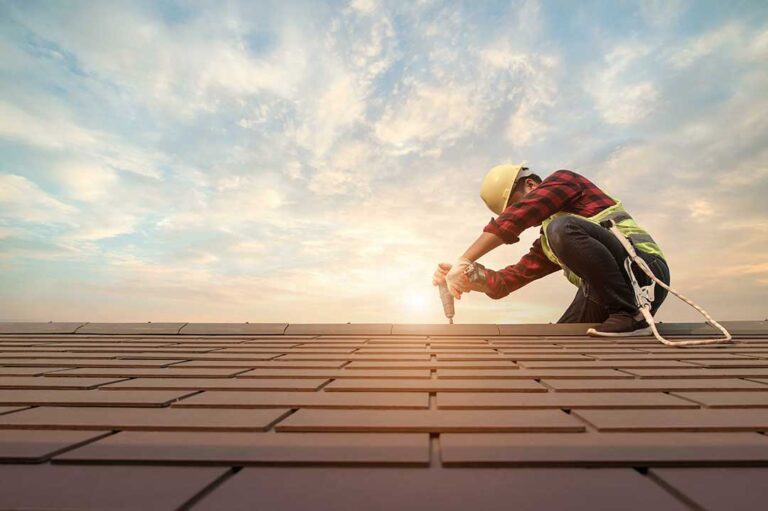 A person using a roller to apply white roof coating to a flat home roof on a sunny day.