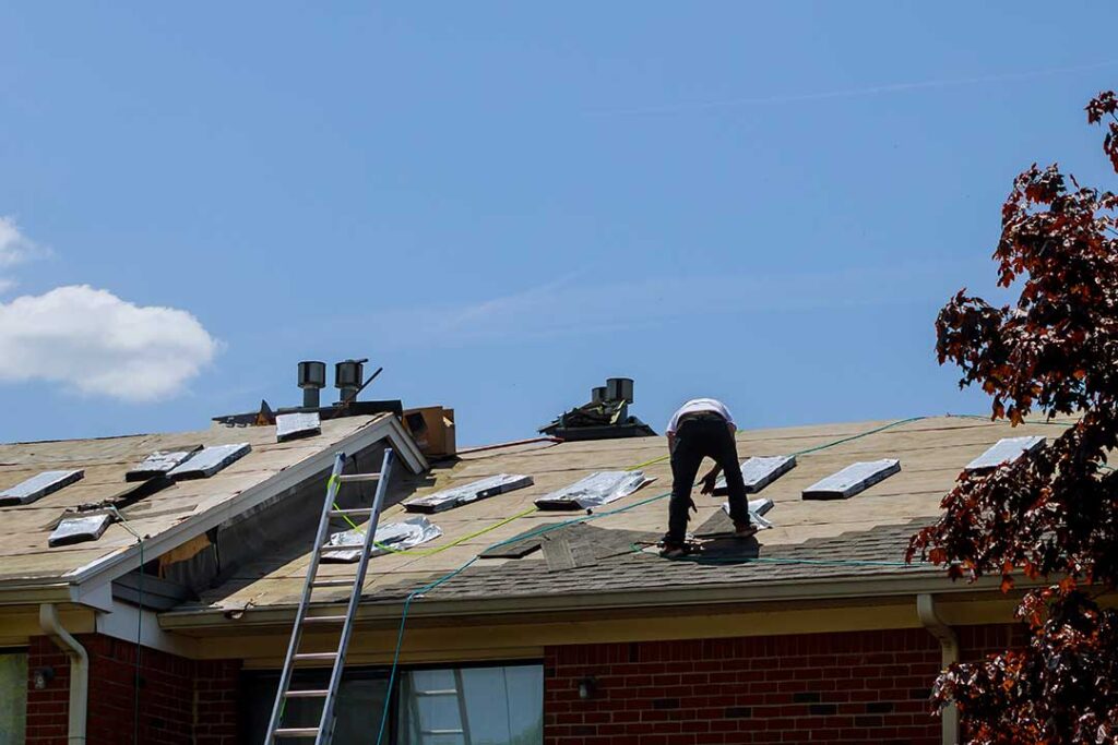 A roofer applies a light-colored, reflective material to a residential roof on a sunny day.