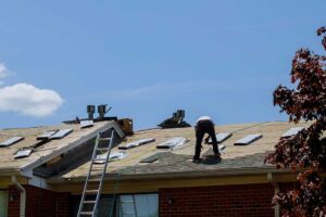 A roofer applies a light-colored, reflective material to a residential roof on a sunny day.