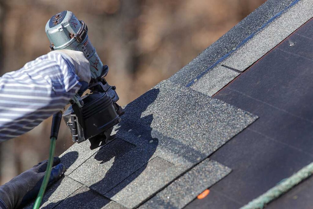 A shingled roof with a raised cricket behind a masonry chimney directing water around both sides.